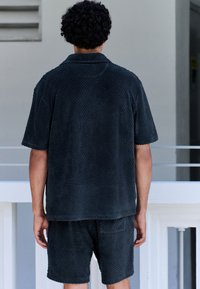 Completo scuro con maglietta a maniche corte e pantaloncini, caratterizzato da un motivo a diamante. Tessuto morbido con vestibilità comoda e bordi leggermente sfilacciati.