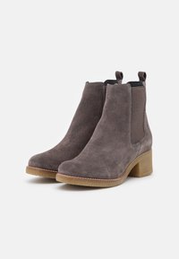 Bottines en daim grises avec un talon carré. Elles présentent des panneaux latéraux élastiques et une surface douce et texturée. Cousu notable autour de la semelle.