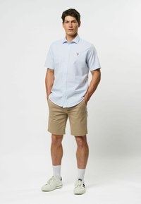 Lichtblauwe, korte-mouwen, knoopsluiting shirt met een subtiel patroon, kaki korte broek, witte sneakers en witte sokken. Minimalistisch ontwerp.