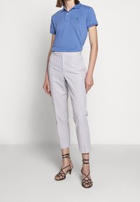 Blå pikétröja med en grön logotyp, kombinerad med ljusrandiga skräddarsydda byxor och svarta remsandaler med hög klack.