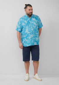 Korte mouwen, knoopje omhoog shirt in helderblauw met een wit palmbladpatroon, gecombineerd met donkerblauwe shorts en off-white sneakers.