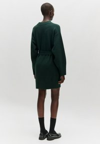 Dunkelgrünes Strickkleid mit einem Taillengürtel, langen Ärmeln und gerippten Bündchen, das bis zur Mitte des Oberschenkels reicht. Einfaches, strukturiertes Design.