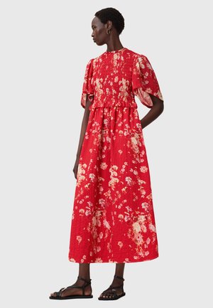 Röd blommig maxiklänning med korta fladderärmar, rynkad bodice och en flödande kjol. Har en texturerad tyg med smockad midja.