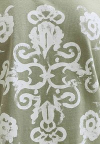 Λευκό φθαρμένο λουλουδένιο και κυματιστό μοτίβο σε φόντο ελιάς πράσινου υφάσματος με υφή.