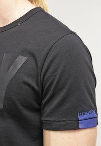 Black short-sleeve t-shirt with a large black "Y" design on the front and a small blue "REPLAY" accent on the sleeve. Soft cotton fabric.