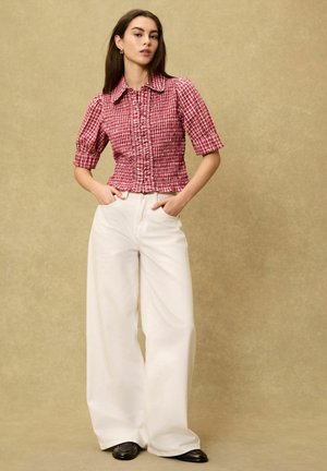 Rød- og hvidternet kortærmet bluse med en rynket tekstur, kombineret med højtaljede, vidde hvide bukser og sorte sko.