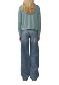 Hellblauer Strickpullover kombiniert mit weit geschnittenen blauen Jeans. Die Jeans verfügen über Gesäßtaschen und haben eine ausgewaschene Optik.