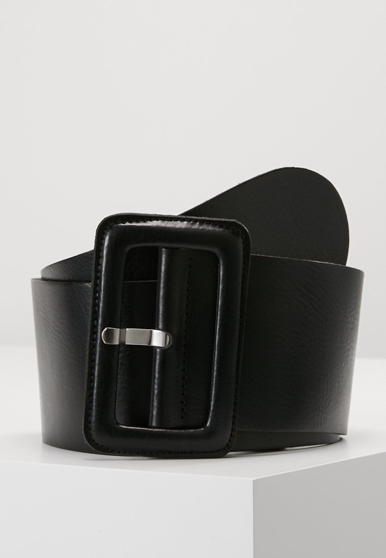 Large ceinture en cuir noir avec une grande boucle rectangulaire rembourrée et ardillon argenté, présentée enroulée sur une surface blanche.