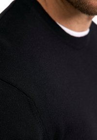 Maglione nero a maglia con scollo rotondo, texture a costine e dettagli di cucitura visibili sulla cucitura della spalla.