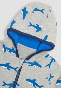 Grijze hoodie met blauwe haai print. Voorzien van een blauwe binnenslip en een rits aan de voorkant. Gemaakt van zacht katoen met ribgebreide randen.