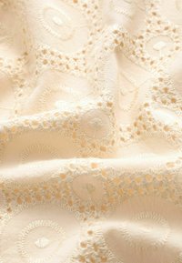Beige bestickter Stoff mit kreisförmigen und floralen Mustern, einer weichen Textur und kunstvollen Nähdetails.