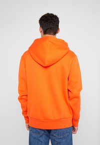 Orange huva sweatshirt i mjukt tyg, med en kenguruficka och ribbade muddkanter, bärs över blå jeans.