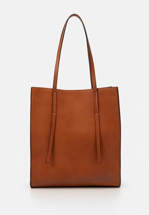 Sac cabas en cuir marron avec de longues bretelles d'épaule et une surface lisse et unie, debout sur un fond blanc.