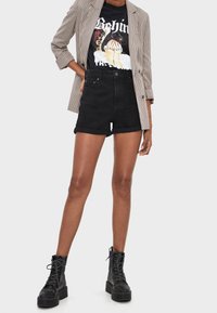Person wearing black high-waisted rolled shorts, graphic black t-shirt, checkered blazer, and black lace-up platform boots.