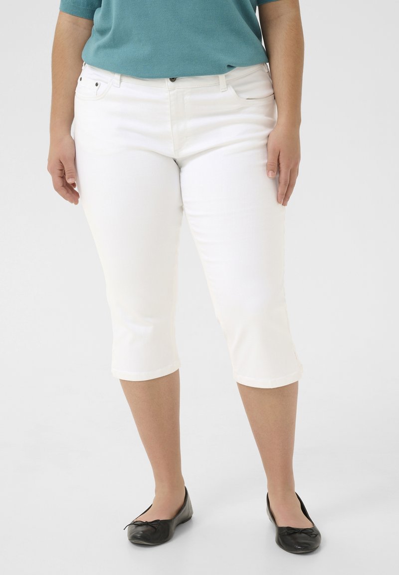 Jean blanc court avec une coupe slim, en denim. Doté d'un design classique à cinq poches et assorti d'une chaussure plate noire.