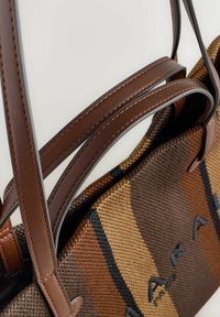 Taška na rameno s textúrovanou hnedou tkanou látkou s oranžovými a čiernymi pruhmi, doplnená hnedými koženými remienkami a embosovaným logom.