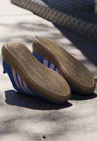 Blue sneakers with light pink stripes, soles facing up, resting on sunlit concrete surface with shadows.