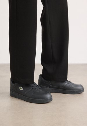 Zwarte lage sneakers van glad leer, met een gestructureerde rubberen zool, vetersluiting en een klein groen geborduurd logo.