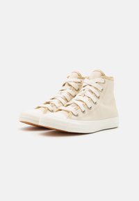 Beiga hög-top sneakers med vita gummisulor, rund tå och krämfärgade snören. Texturerad tyg och en krage med gulddetaljer.