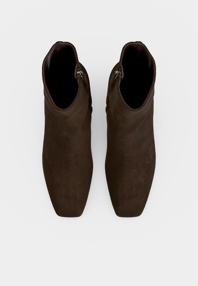 Paire de bottines marron foncé à bouts carrés avec fermetures éclair latérales, vues de dessus sur un fond clair uni.