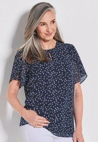 Navy blauwe blouse met korte doorschijnende mouwen, voorzien van een gestippeld patroon in lichtgrijs en een keyhole halslijn. Zachte stof en een ontspannen pasvorm.