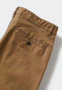 Pantalon en coton marron avec une poche passepoilée à l'arrière fermée par un seul bouton noir et des passants de ceinture sur la taille.