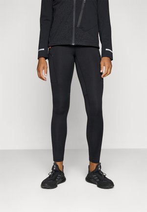 Tenue de sport noire composée de leggings ajustés avec une poche latérale, accompagnée d'une jacket noire ornée de motifs géométriques discrets et d'accents réfléchissants.