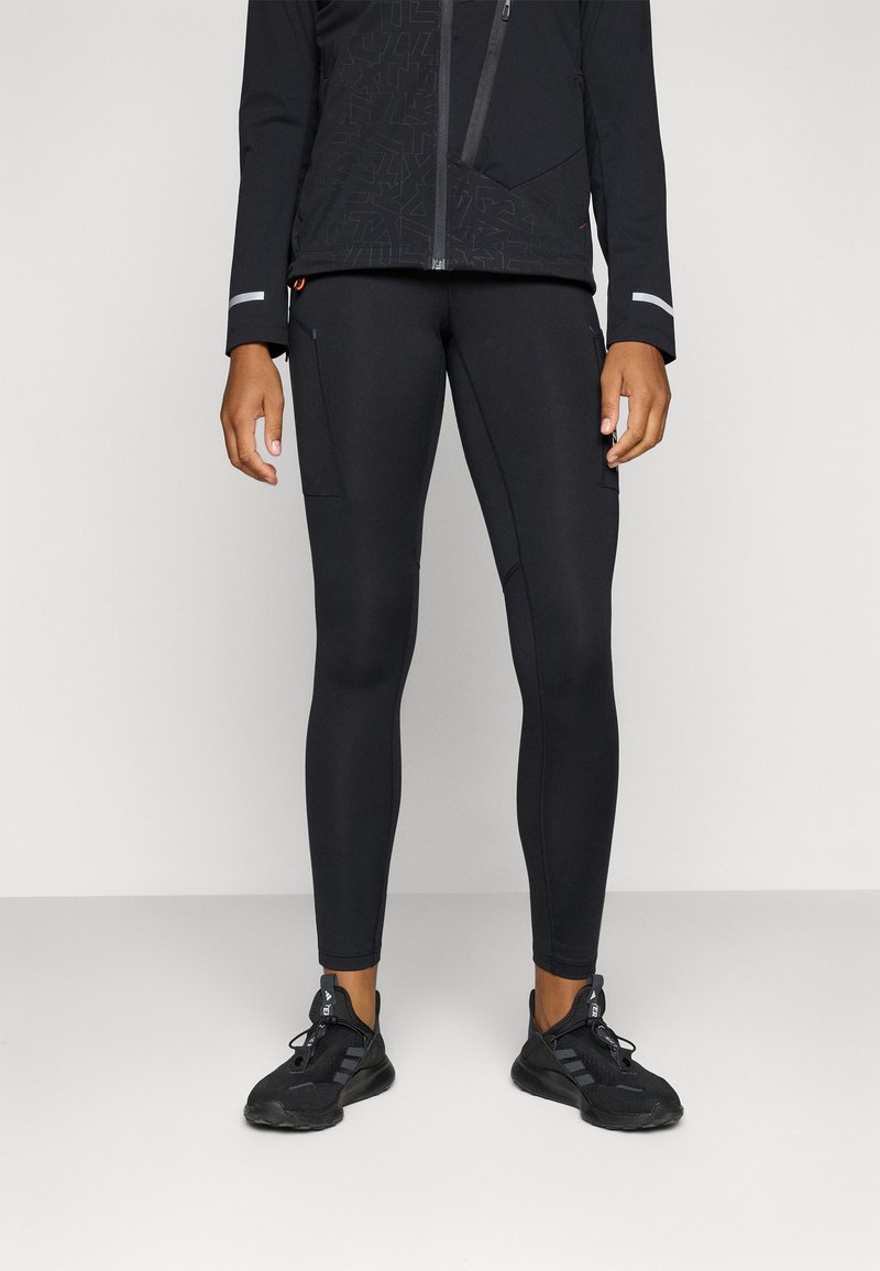 Tenue de sport noire composée de leggings ajustés avec une poche latérale, accompagnée d'une jacket noire ornée de motifs géométriques discrets et d'accents réfléchissants.