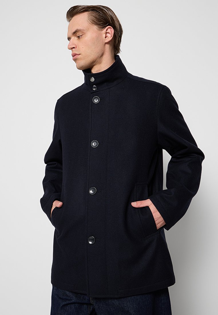 Cappotto di lana blu navy con colletto alto, chiusura frontale a bottoni e due tasche laterali, caratterizzato da una texture liscia e un design classico.