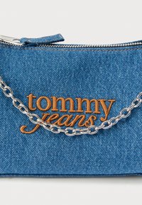 Traper torbica s narančastim vezom "tommy jeans", srebrnim lančanim remenom i zatvaračem na patentni zatvarač. Teksturirani plavi materijal s vidljivim šavovima.