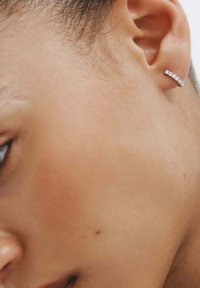 Pendiente de aro de plata con un diseño recto, que presenta pequeñas piedras transparentes engastadas a lo largo del frente. Primer plano de la oreja.