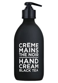 Bouteille noire mate pour crème pour les mains avec un distributeur à pompe. Le texte blanc indique "CRÈME MAINS THE NOIR CRÈME POUR LES MAINS THÉ NOIR". Forme ronde et texture lisse.
