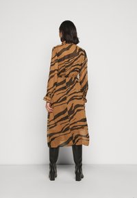 Abito marrone a maniche lunghe con strisce tigre nere, vita cintrata, silhouette fluida e tessuto strutturato, abbinato a stivali neri al ginocchio.
