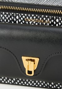 Melnā struktūrētā maks ar austu melnas un baltas auduma detaļu. Aprīkots ar zelta metāla detaļām, trīsstūra aizdari un nospiestu logotipa detaļu.