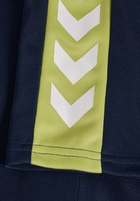 Granatowe krótkie spodenki sportowe z zielonym paskiem i białymi akcentami w kształcie srego. Tkanina ma teksturowane wykończenie, podkreślające kontrast wzoru.