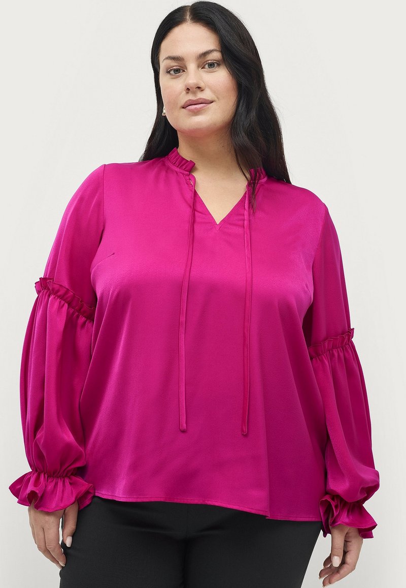 Fuchsia satin bluse med v-hals, samlede ærmer og flæser ved håndleddene. Stofret er glat, hvilket skaber en flydende silhuet.