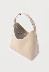 Μπεζ τσάντα χειρός από δέρμα με έναν ρυθμιζόμενο ιμάντα, ανοιχτό πάνω μέρος και εσωτερική τσέπη με φερμουάρ, φωτογραφημένη σε λευκό φόντο.