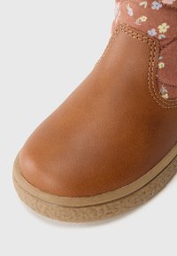Braune Lederknöchelstiefel mit strukturiertem Gummisohle, floralen Stoffakzenten oben und genähten Details entlang der Ränder.