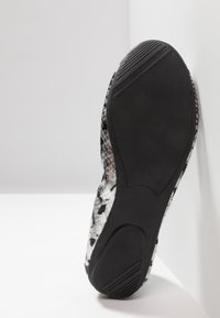 Suola di una scarpa con una base in gomma nera testurizzata, caratterizzata da un motivo in pelle di serpente argento e nero sul lato superiore.