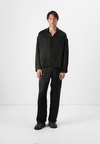 Chemise noire à manches longues, coupe décontractée, avec une fermeture à boutons sur le devant et un pantalon large assorti. Texture douce, design décontracté et style minimaliste.