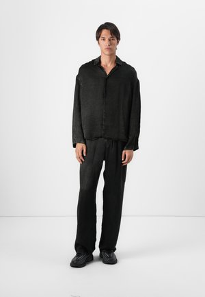 Black, relaxed-fit long-sleeve shirt with a button-up front and matching loose trousers. Soft texture, casual design, and minimalistic style.