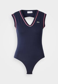 Laivaston värinen bodysuit, jossa on V-pääntie ja hihattomat hihat, punaisia yksityiskohtia. Lacosten logo vasemmassa rinnassa. Valmistettu sileästä, joustavasta materiaalista.
