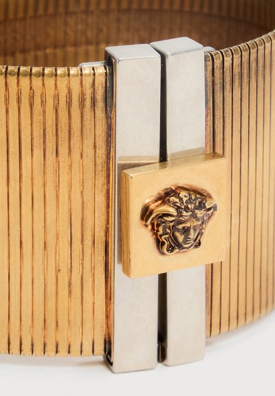 Złocona bransoletka o rowkowanej fakturze z srebrną klamrą, ozdobioną małym złotym kwadratem z wytłoczonym emblematem głowy Meduzy.