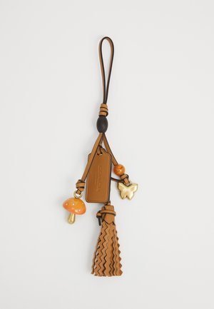 Leather wristlet keychain with tassel, orange mushroom charm, gold butterfly charm, and rectangular tag embossed with "Coach New York."