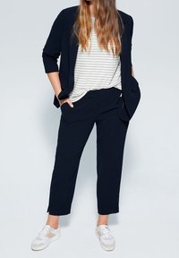 Námořnické sako a kalhoty stejné barvy s volným střihem, doplněné proužkovaným bílým tričkem a bílými teniskami s béžovými detaily.