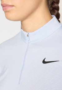 Camicia a maniche lunghe a righe blu chiaro con colletto alto e zip a metà; presenta il logo Nike nero sul petto.