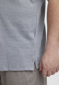 Szürke, rövid ujjú ing textúrált anyagból, oldalsó hasítékokkal az alján és laza szabással, világos színű nadrággal párosítva.