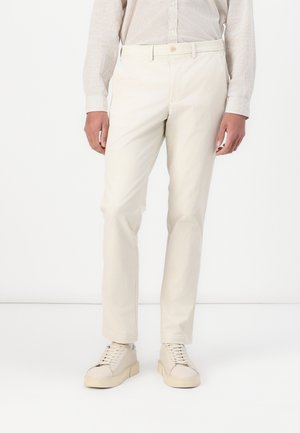 Beige cotton trousers with a straight cut, featuring belt loops and a button closure. Paired with light-colored sneakers.