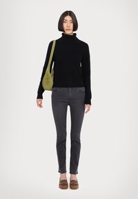 Schwarzer gerippter Rollkragenpullover kombiniert mit dunkelgrauen Slim-Fit-Jeans und braunen Slippern. Accessoires bestehen aus einer grünen Wildleder-Schultertasche.