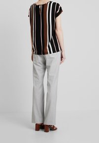 Top nero con righe verticali in marrone, rosa e bianco; maniche corte e dettaglio a chiave sul retro. Abbinarlo a pantaloni grigi chiari.